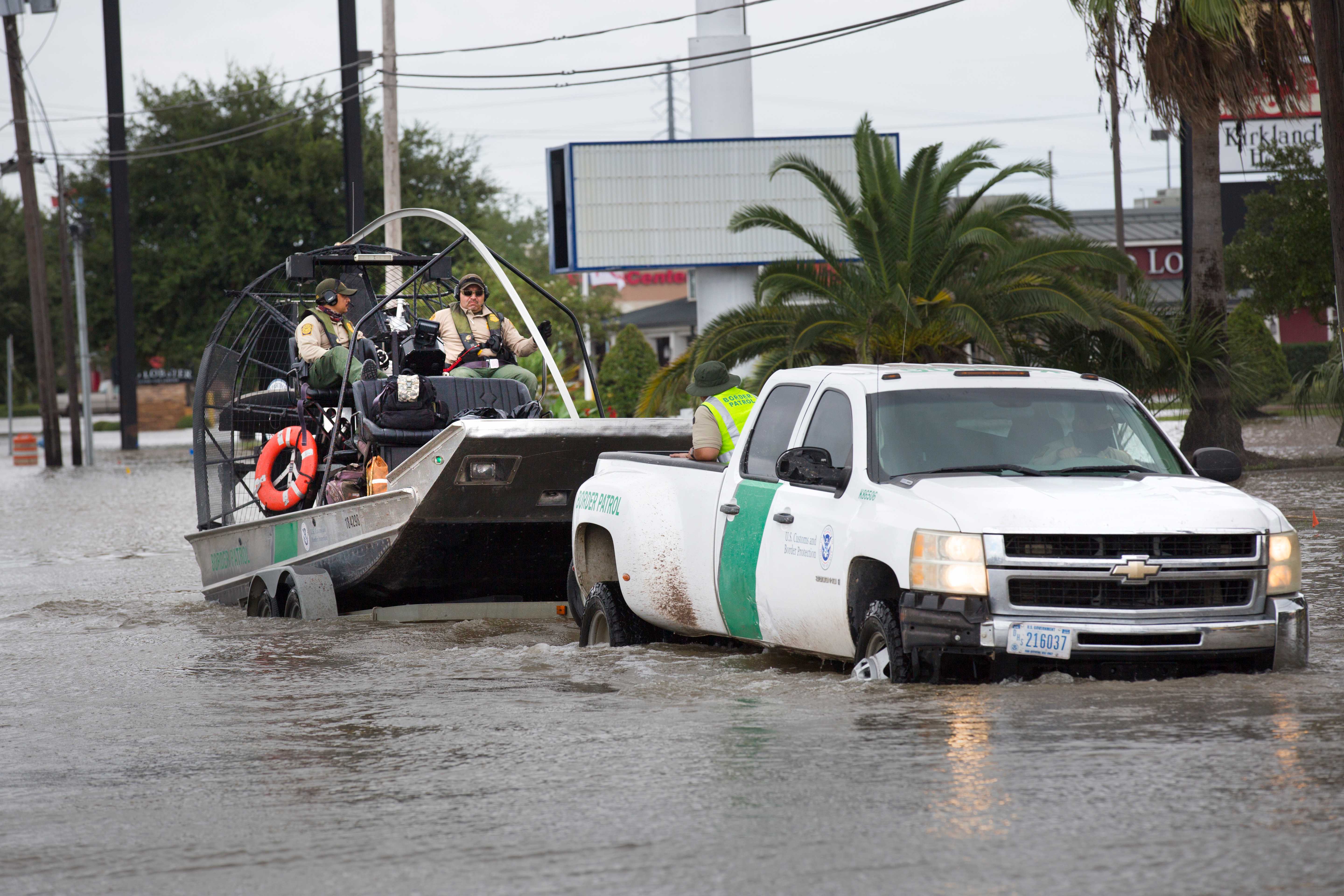 A picture of a pickup truck towing an airboat in high flood waters with two rescuers in the airboat with life vests